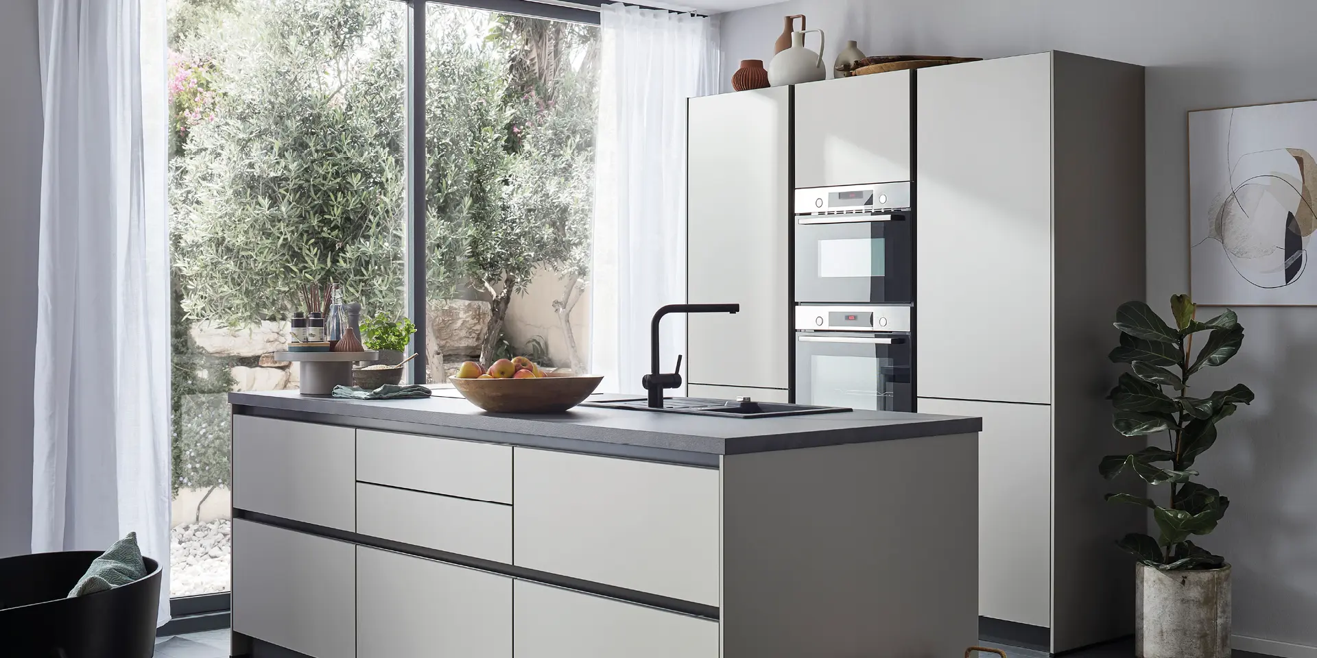 Weiße Küche mit Kochinsel, schwarzen Armaturen, Einbaugeräten und großer Fensterfront